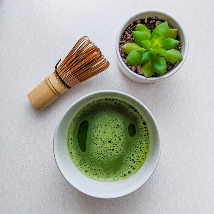 Bowl filled with frothy matcha, and a matcha whisk laying on table